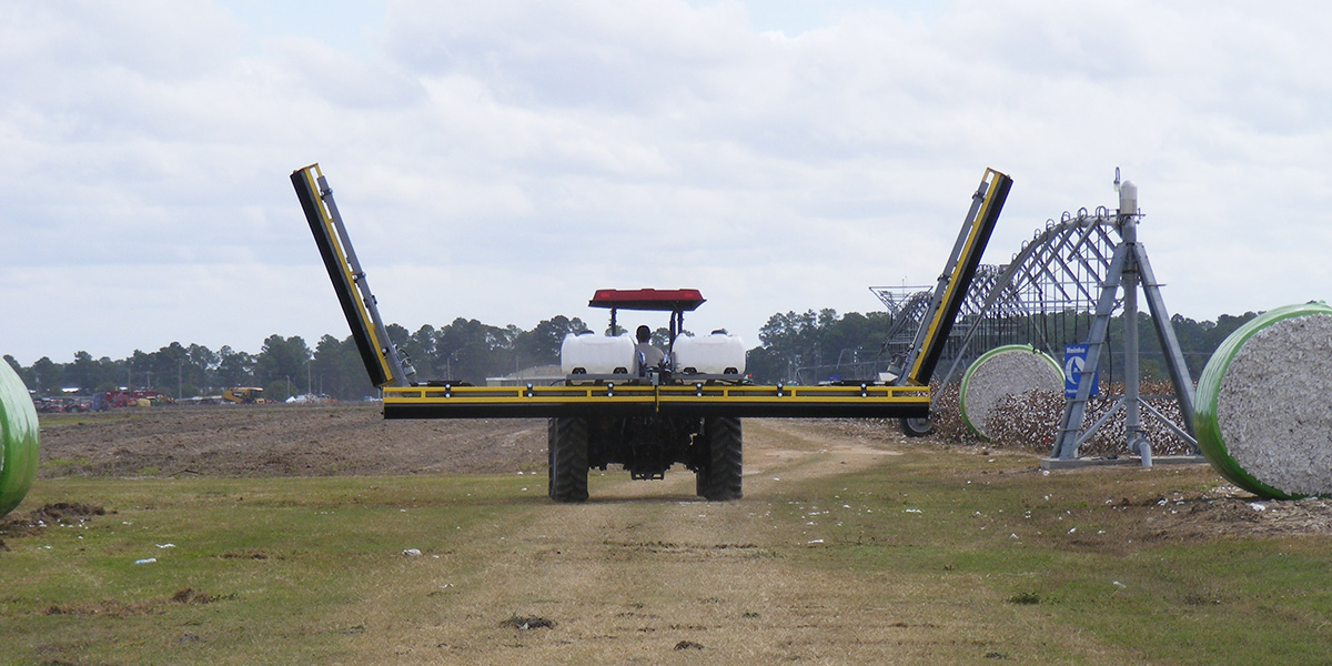 A GrassWorks Flex Unit Weed Wiper mounted on a red tractor, demonstrating its capability in large-scale weed management in cotton fields.