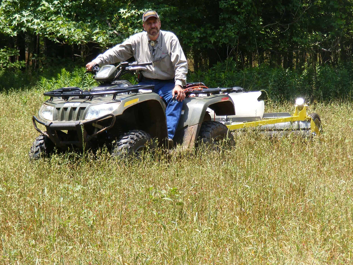 GrassWorks Pull-Type Weed Wiper™ attached to an ATV, wiping tall weeds in a pasture.