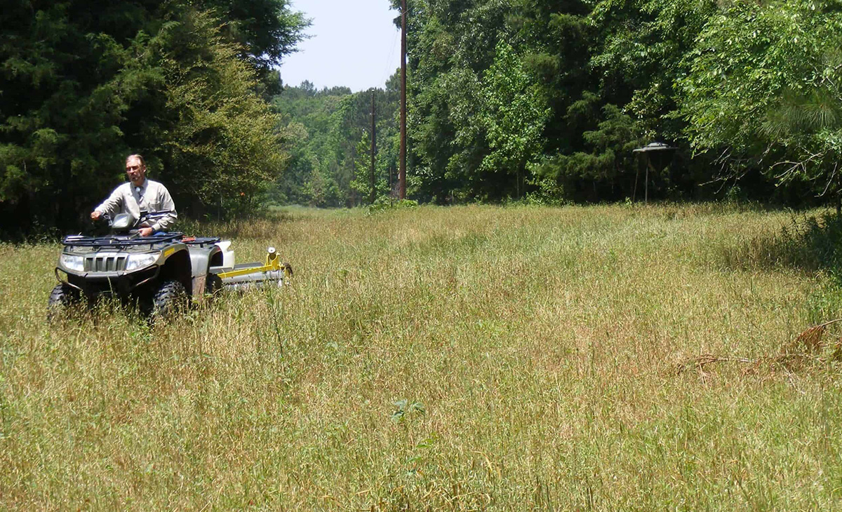 GrassWorks Pull-Type Weed Wiper™ pulled by an ATV, treating overgrown weeds.