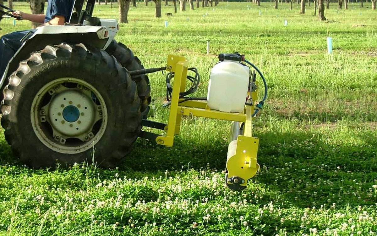 A GrassWorks Weed Wiper attached to a tractor, providing efficient weed control in agricultural and public land settings.
