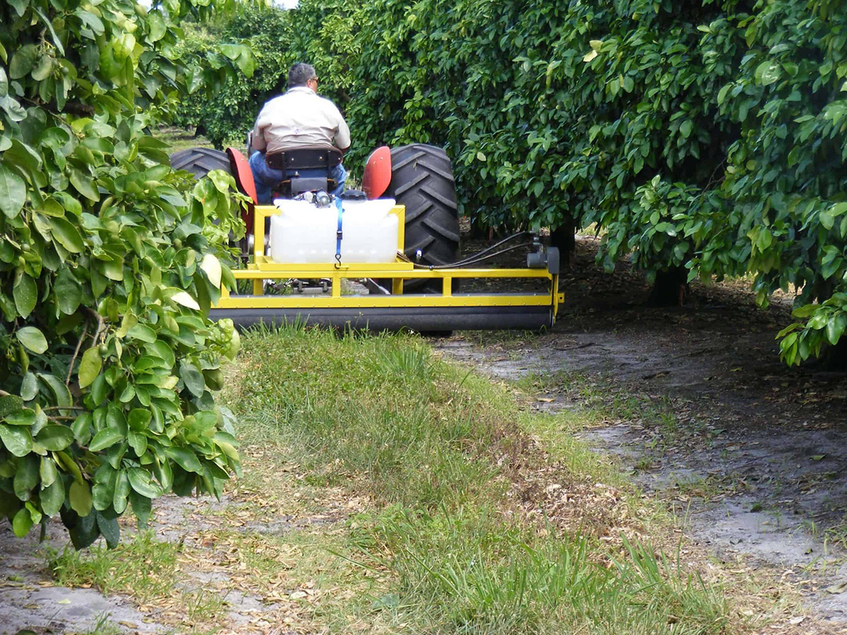 GrassWorks Weed Wiper™ mounted on a tractor, applying herbicide in an orchard between tree rows.