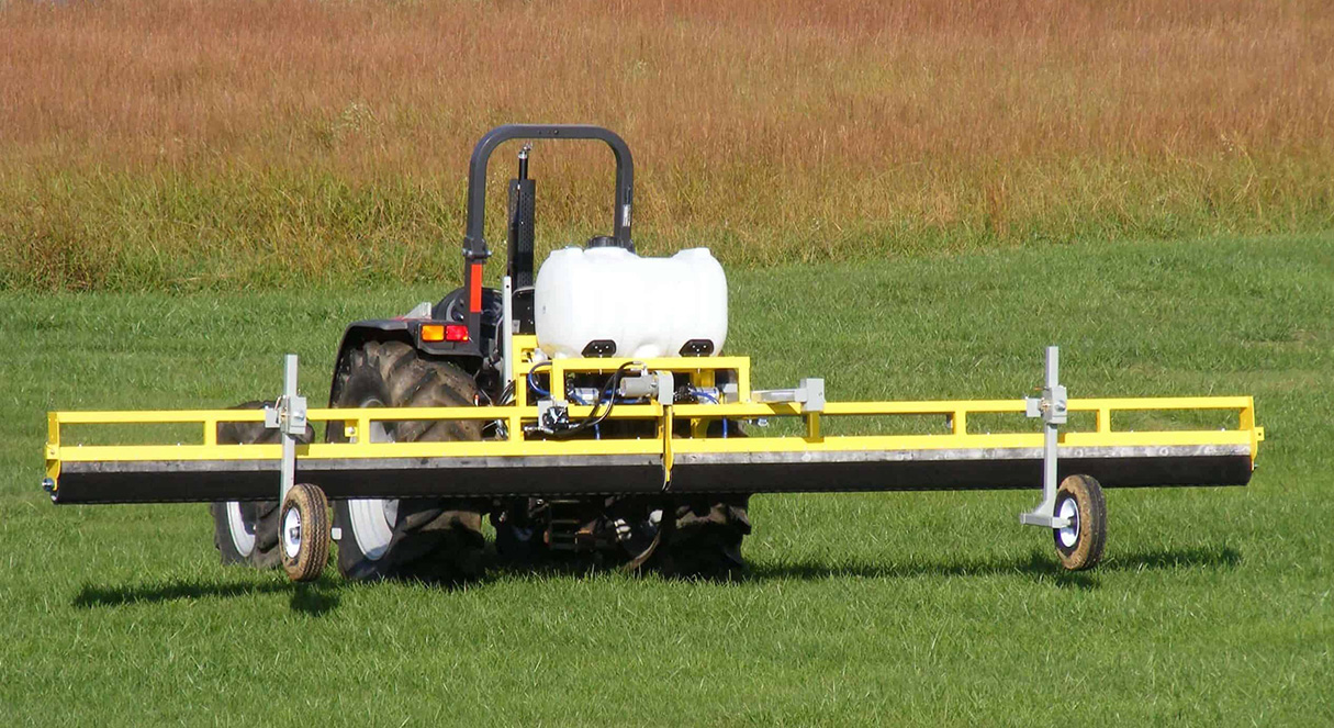 GrassWorks Weed Wiper™ mounted on a tractor, treating weeds in a large green pasture.