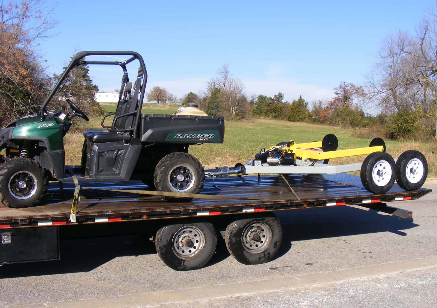 Hydraulic hay bale handler loaded on a flatbed trailer, demonstrating portability and ease of transport for ATV and UTV users.