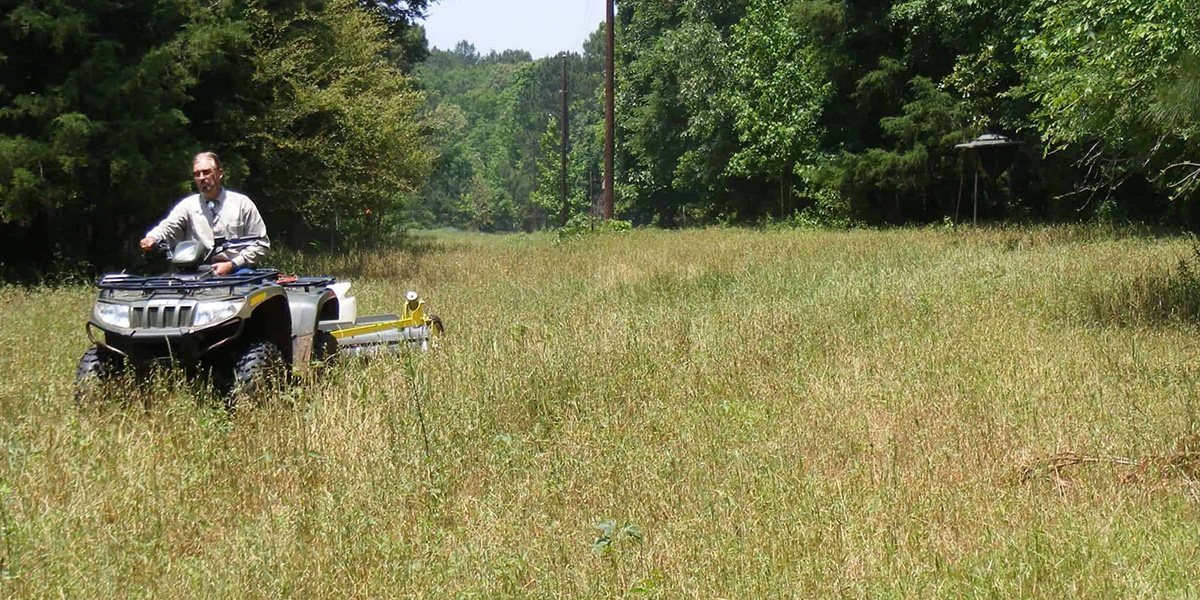 An ATV towing a GrassWorks Pull-Type Weed Wiper across a field, showcasing its cost-effective weed control capabilities.